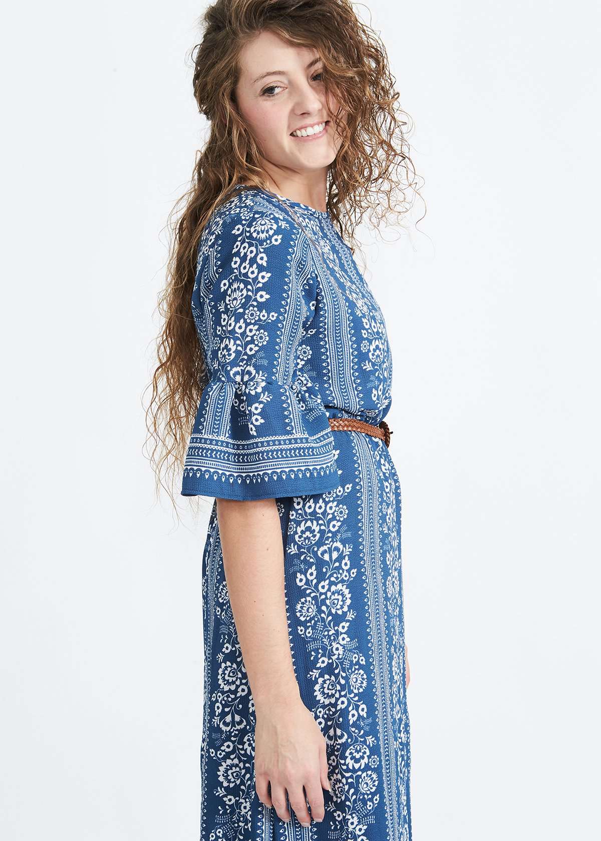 Woman wearing a long bohemian style blue dress with white accent designs and 3/4 trumpet style sleeves.