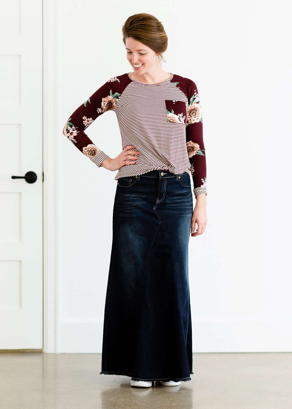 Woman wearing a modest burgandy floral and stripe long sleeve top with a twist front hem.