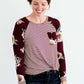 Woman wearing a modest burgandy floral and stripe long sleeve top with a twist front hem.