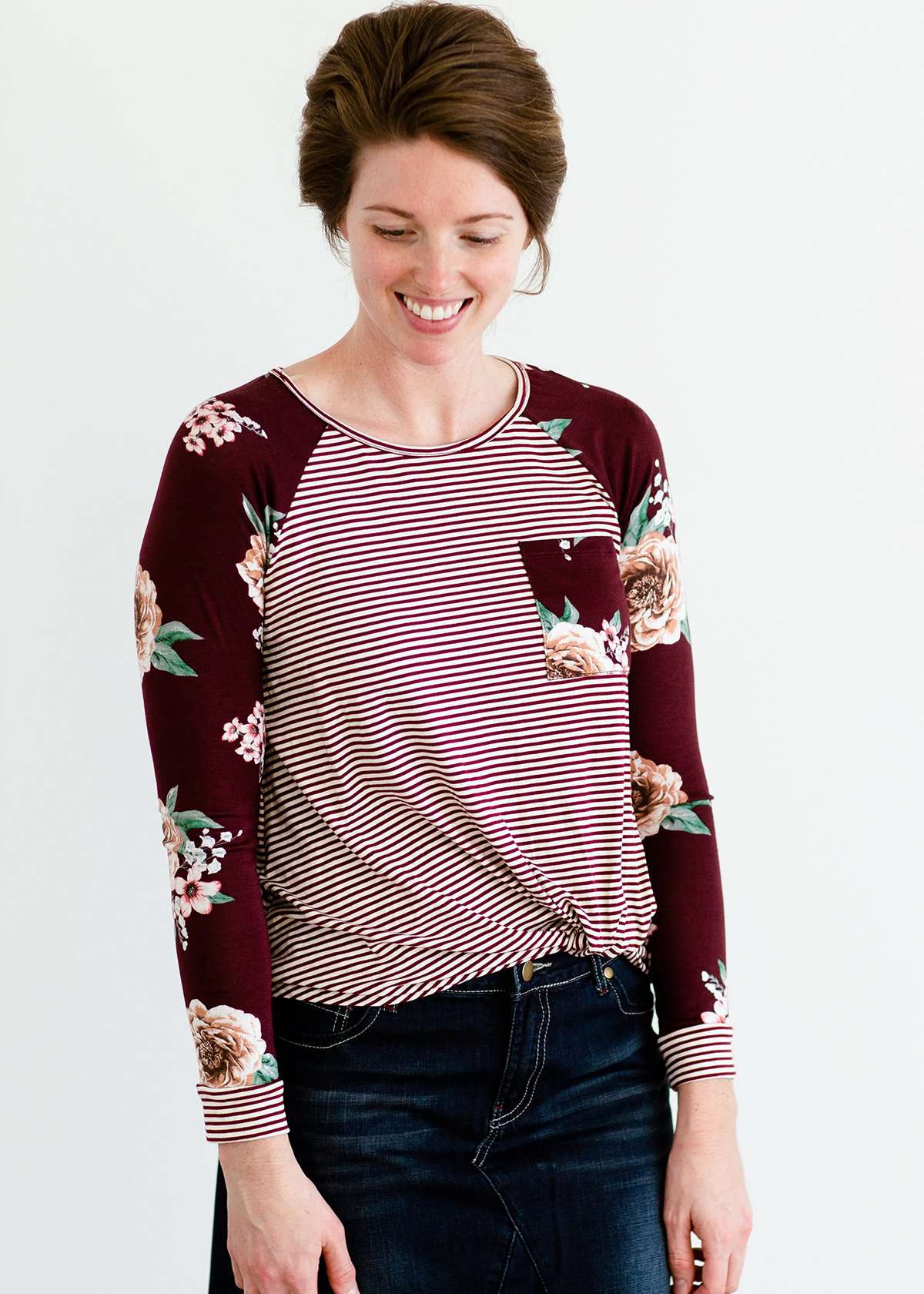 Woman wearing a modest burgandy floral and stripe long sleeve top with a twist front hem.