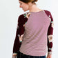 Woman wearing a modest burgandy floral and stripe long sleeve top with a twist front hem.