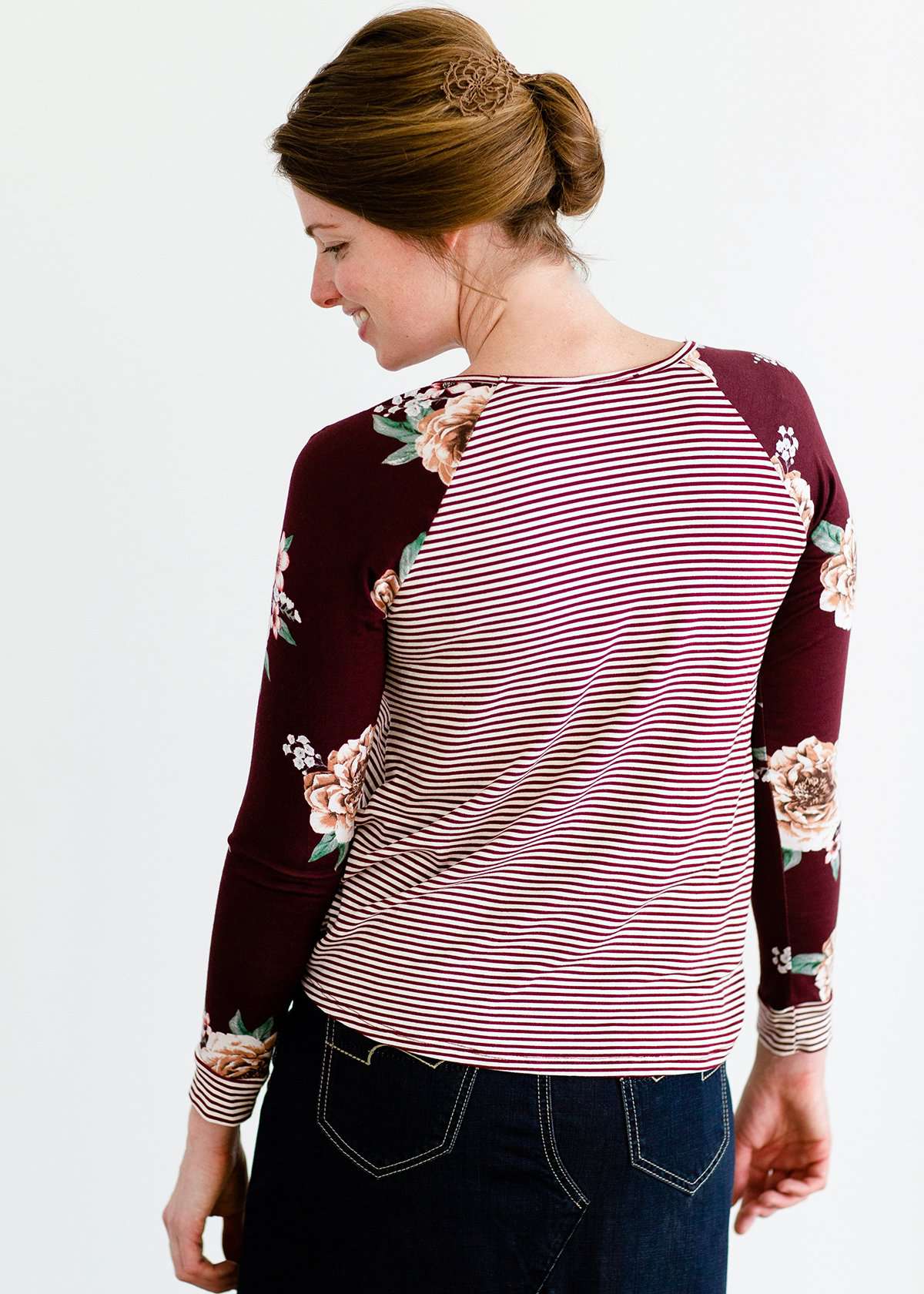 Woman wearing a modest burgandy floral and stripe long sleeve top with a twist front hem.