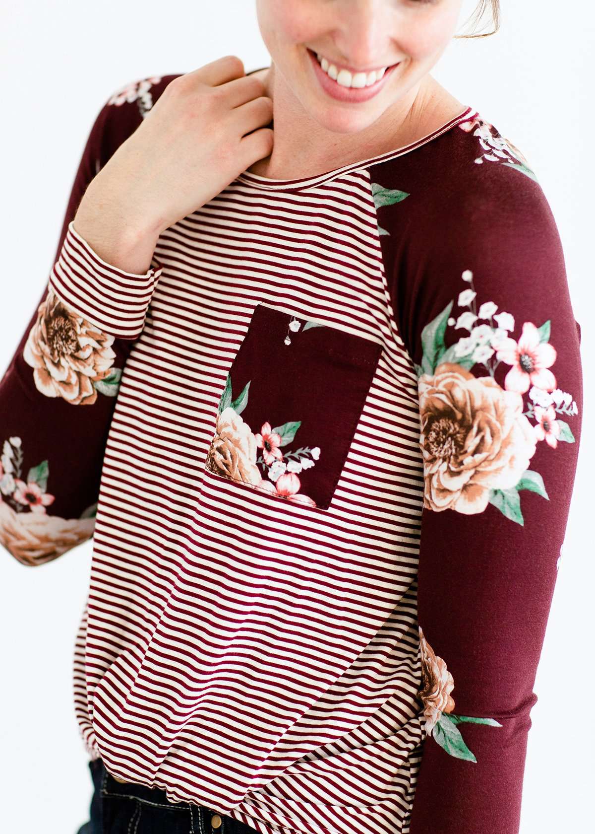 Woman wearing a modest burgandy floral and stripe long sleeve top with a twist front hem.