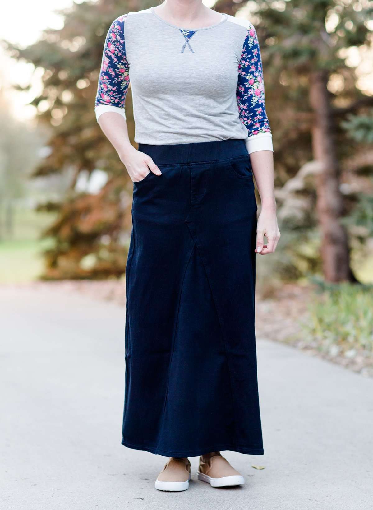 Women wearing a long dark blue denim skirt that is a-line and has flare. This modest skirt is also paired with a floral and gray raglan tee.