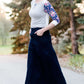 Women wearing a long dark blue denim skirt that is a-line and has flare. This modest skirt is also paired with a floral and gray raglan tee.