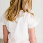 Girl wearing a modest ivory colored tie front top with flutter sleeves