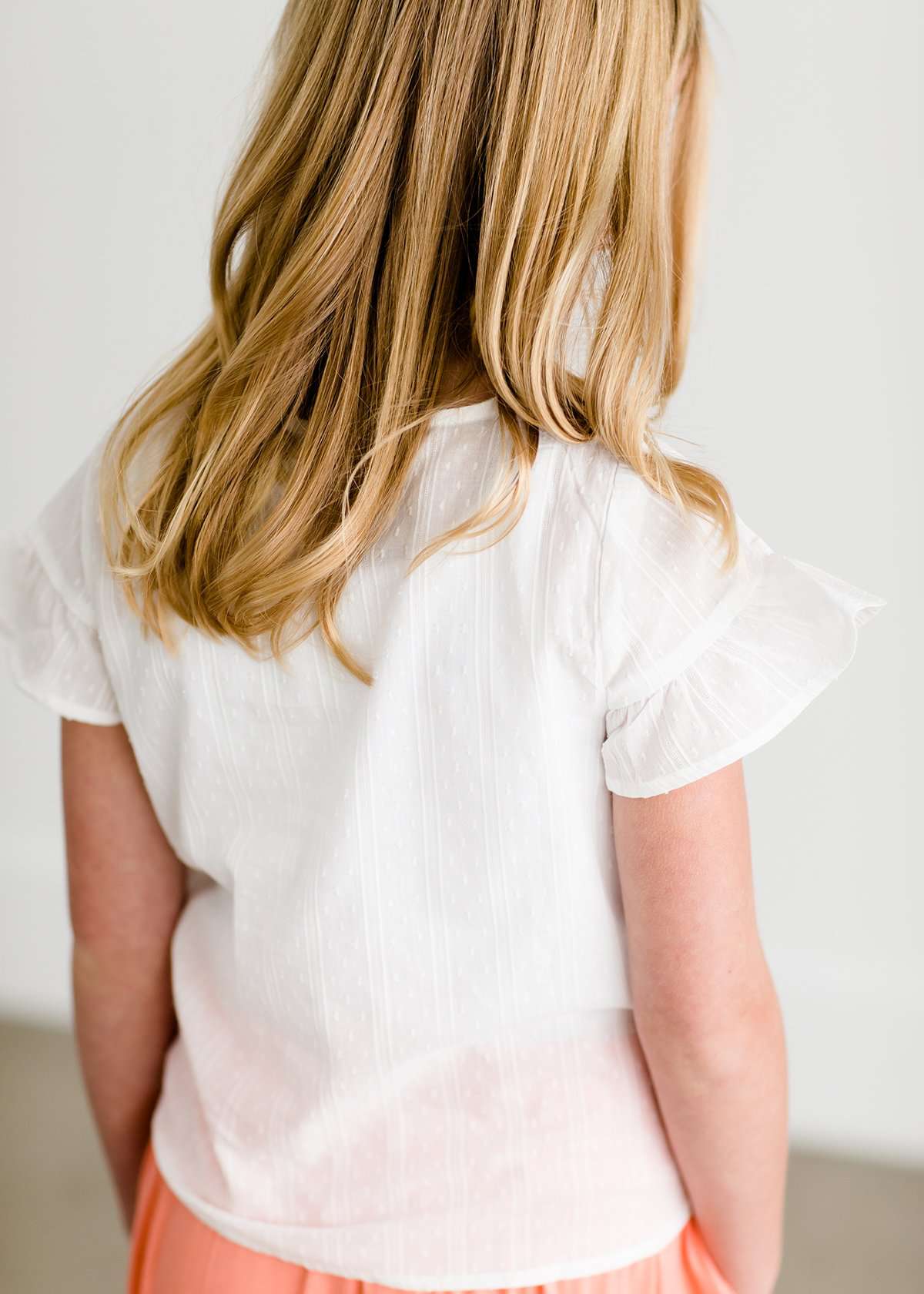 Girl wearing a modest ivory colored tie front top with flutter sleeves