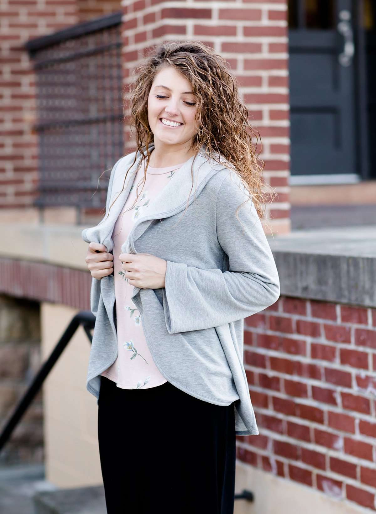 This woman is wearing a tri-blend fleece jacket that is heather gray and has a drape front and shawl collar. 