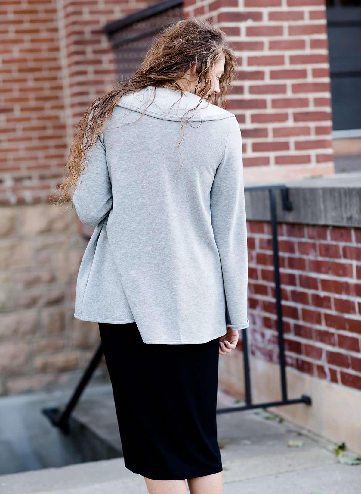 This woman is wearing a tri-blend fleece jacket that is heather gray and has a drape front and shawl collar. 