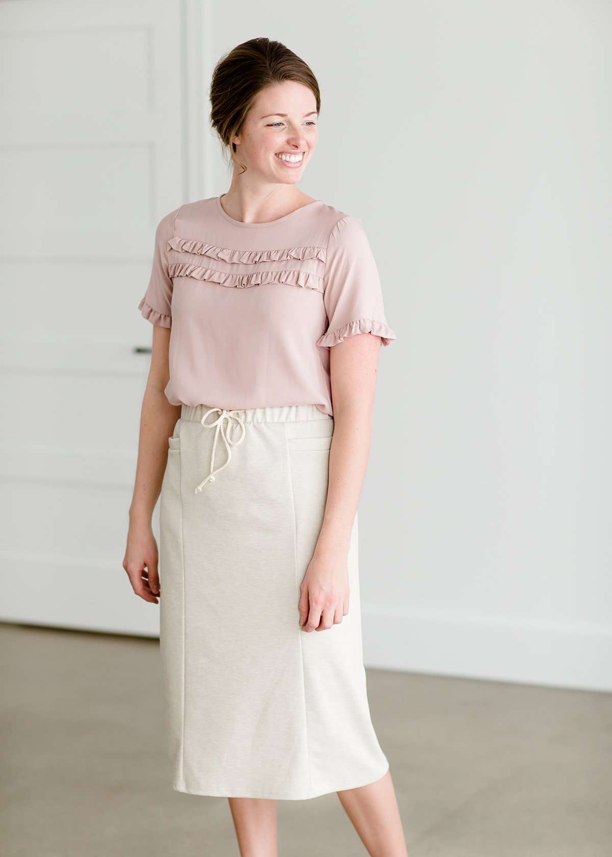Woman wearing a cream colored french terry below the knee skirt with front ties, front panels and pockets!
