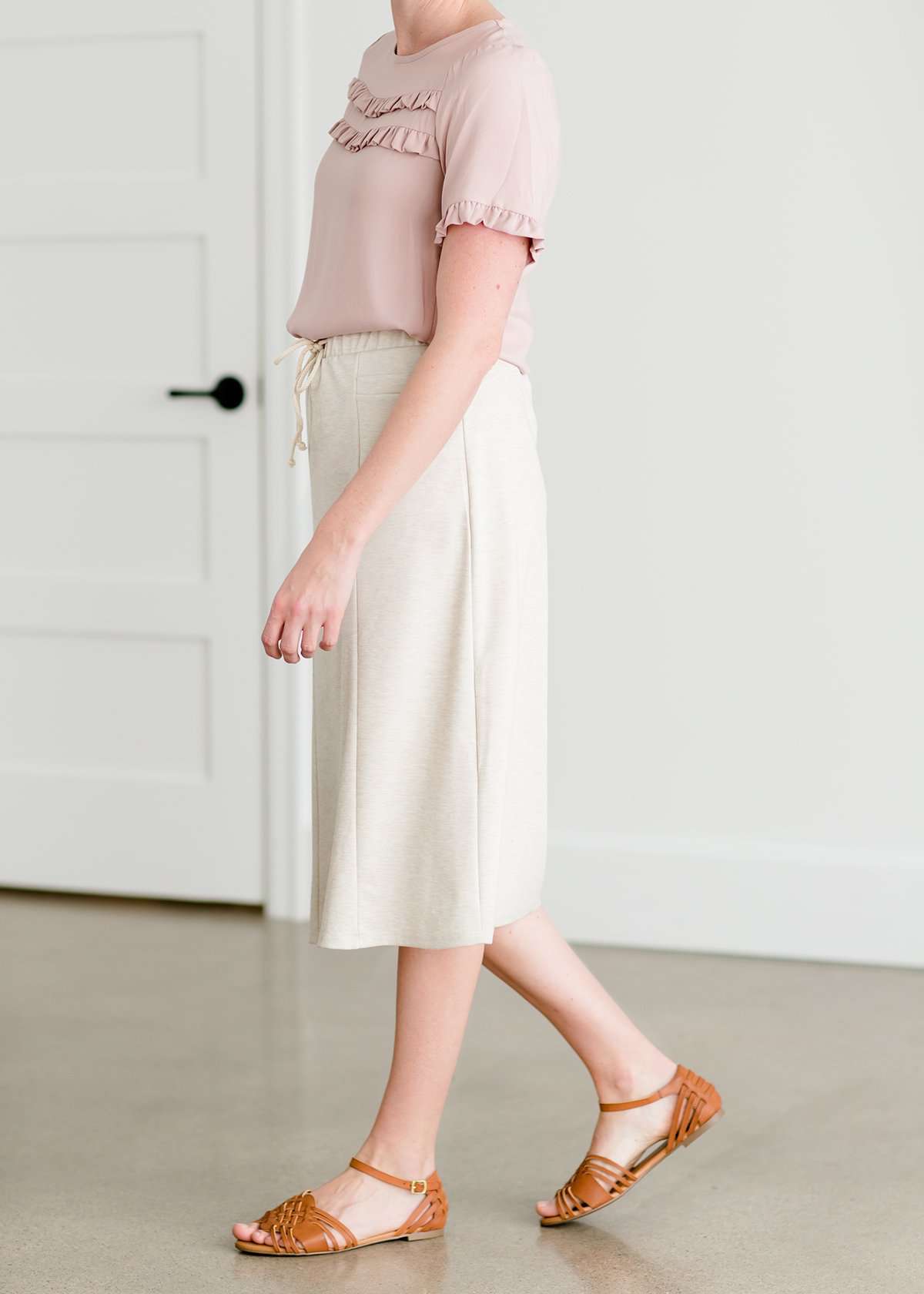 Woman wearing a cream colored french terry below the knee skirt with front ties, front panels and pockets!