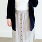 Woman wearing a gray striped skirt with camel colored faux buttons on the front that also has an elastic waistband