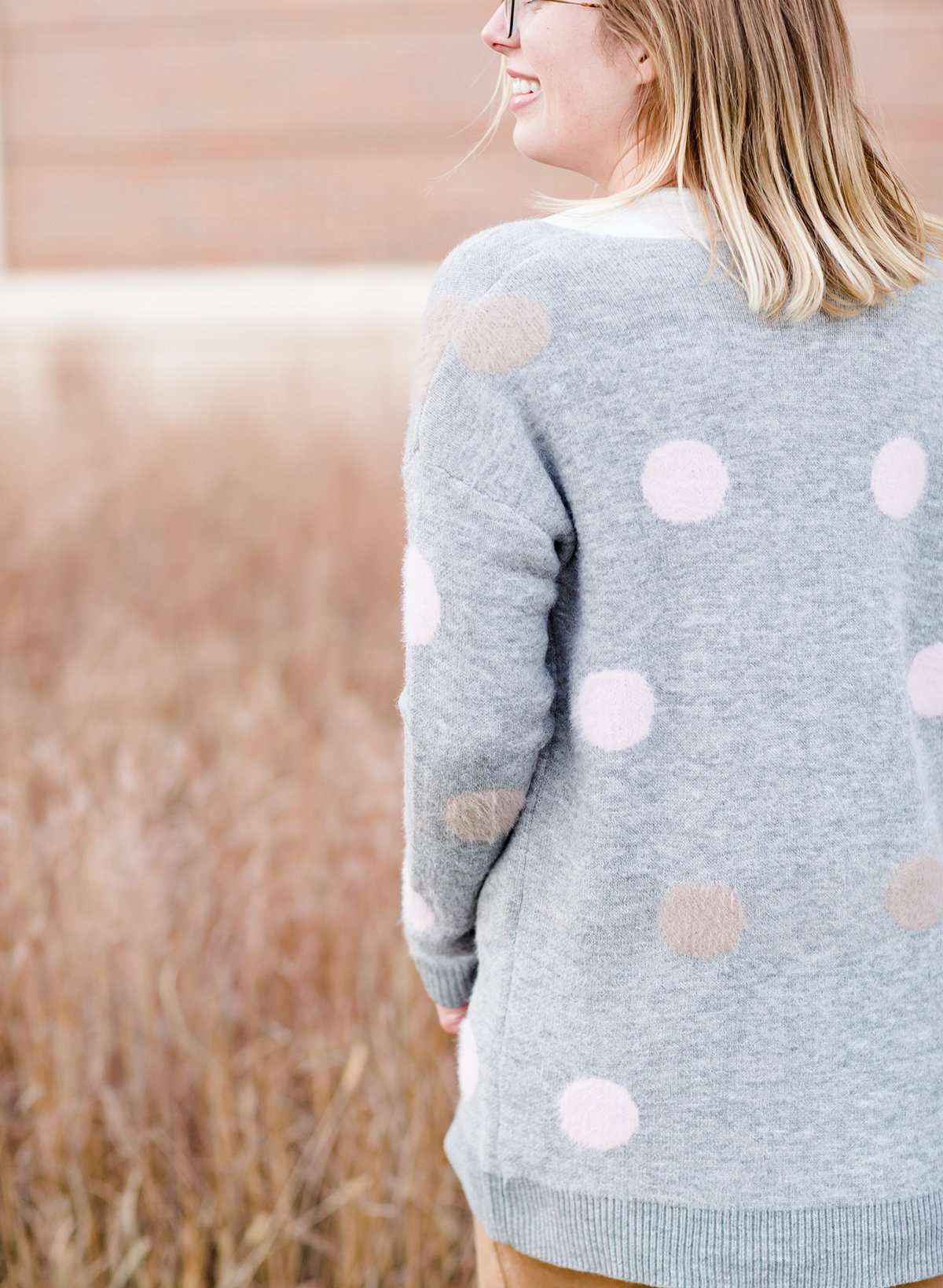 Young woman wearing a modest, long, polka dot, gray, open front cardigan. She is also wearing a khaki corduroy below the knee skirt.