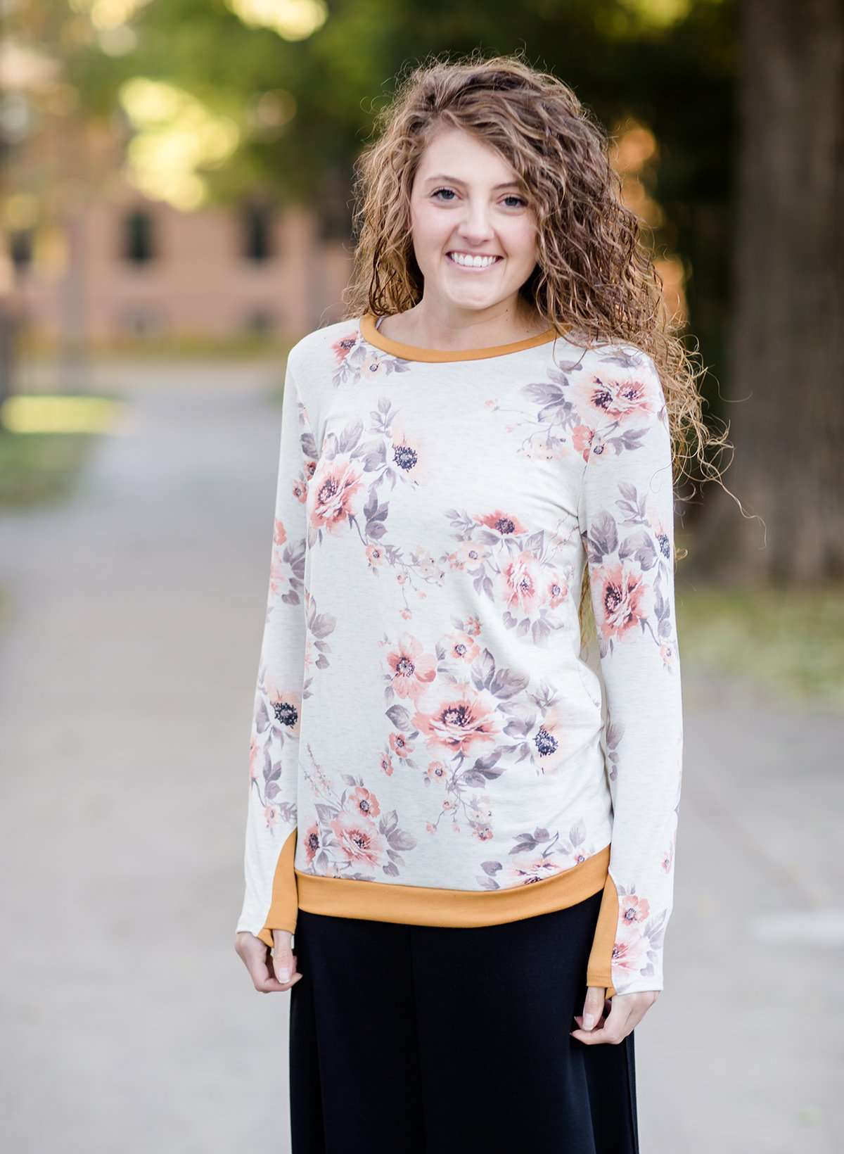 Woman wearing a blush floral modest sweatshirt with thumbholes that is lined with a mustard trim