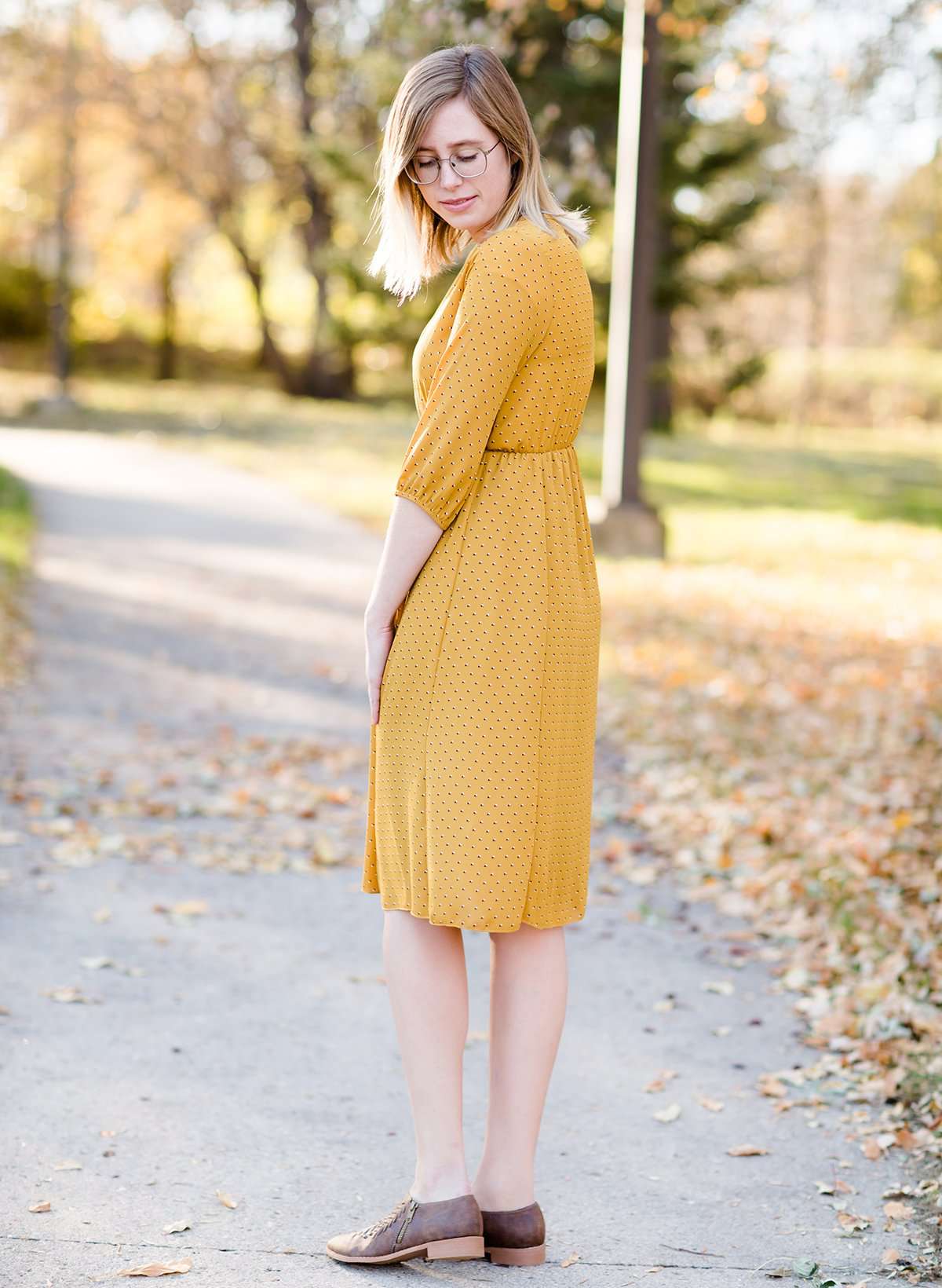 Young woman wearing a modest golden printed midi dress that has a faux wrap and is nursing friendly
