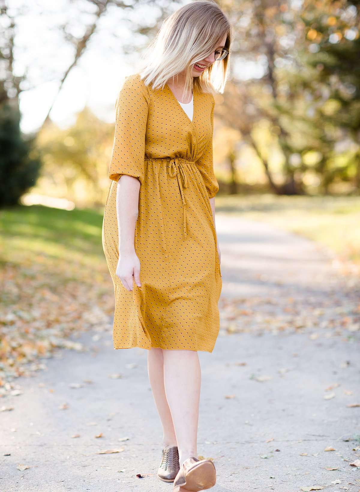 Young woman wearing a modest golden printed midi dress that has a faux wrap and is nursing friendly