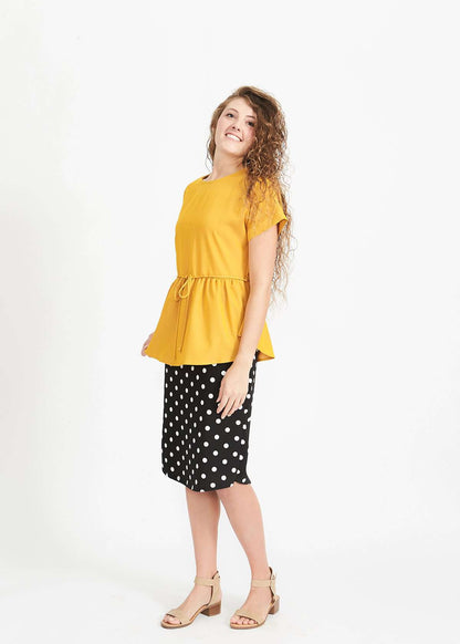 Woman wearing a mustard peplum style blouse with a self tie fabric belt