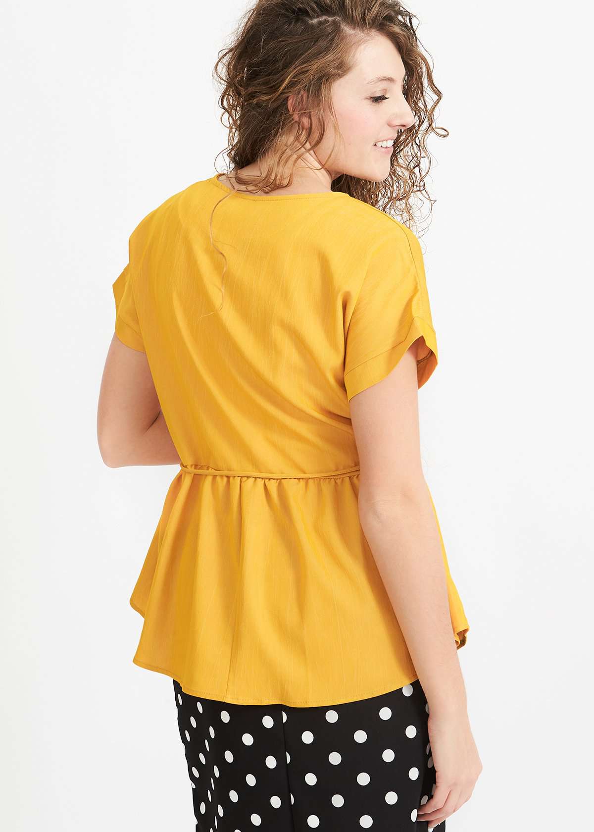 Woman wearing a mustard peplum style blouse with a self tie fabric belt