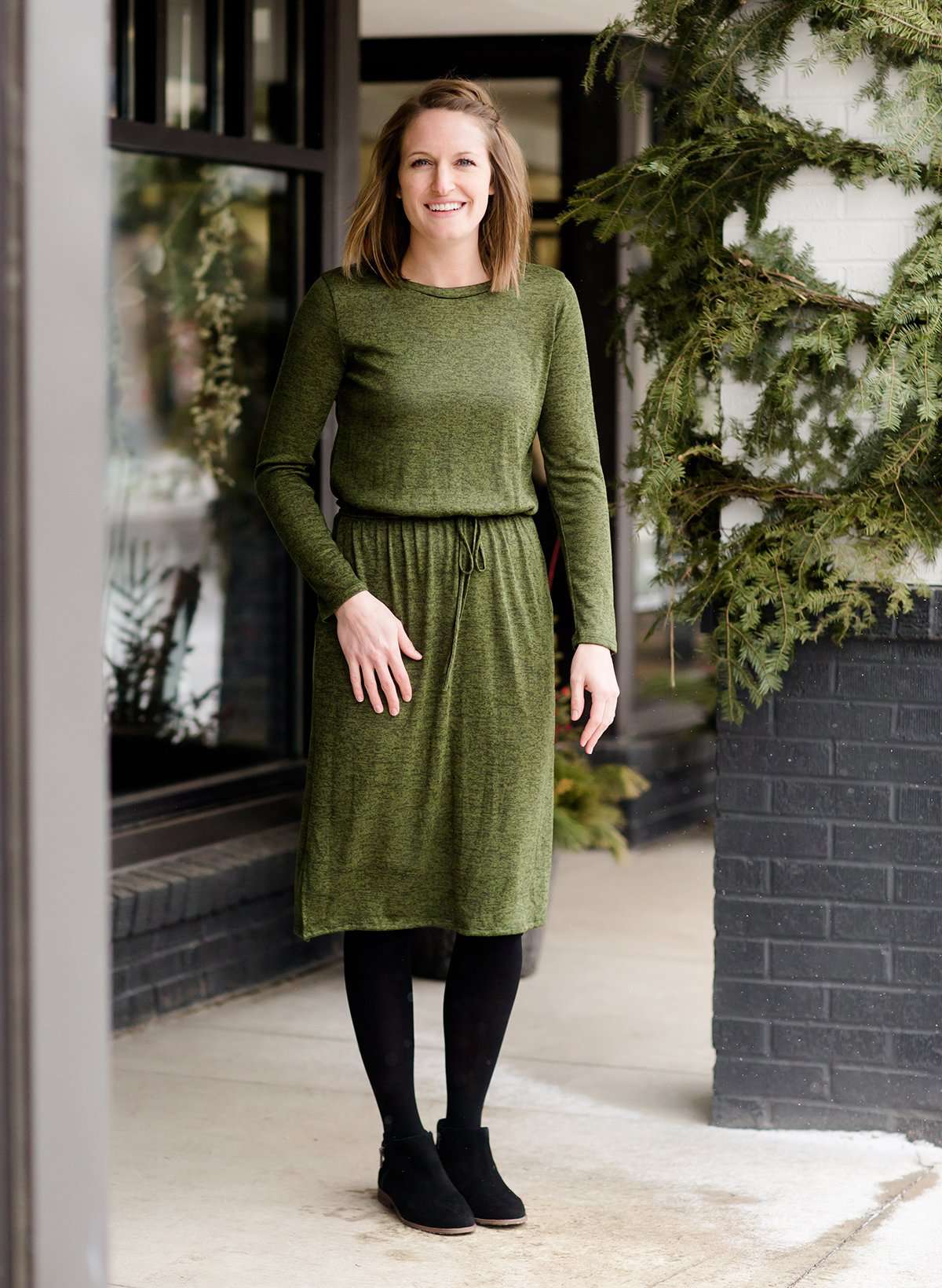 Woman wearing a olive colored hacci midi dress with a elastic waist and paired with black sole society boots