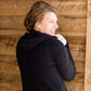 Woman wearing a black, Ampersand half zip, back sweatshirt. It has white toggle strings and a front kangaroo pouch pocket. It is also paired with a long modest jean skirt.