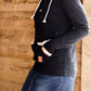 Woman wearing a black, Ampersand half zip, back sweatshirt. It has white toggle strings and a front kangaroo pouch pocket. It is also paired with a long modest jean skirt.
