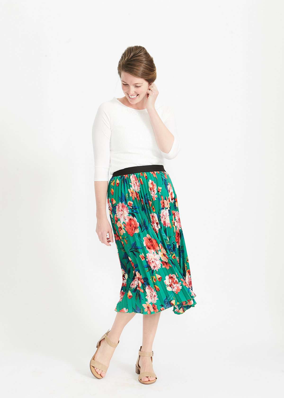 Woman wearing an emerald green floral stretchy pleated swing skirt with dress shoes and a white lace top
