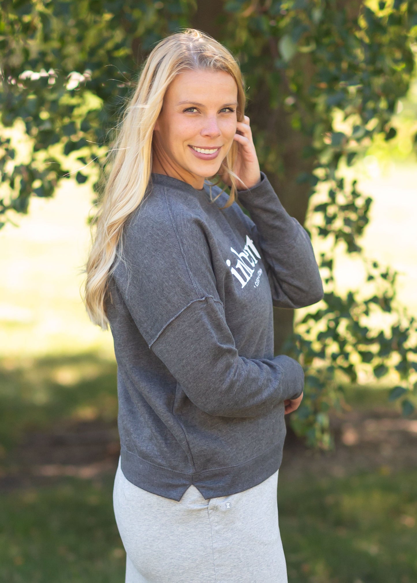 Inherit Crew Neck Sweatshirt Tops come in charcoal, blush pink, or hearthered light grey. They have white Inherit logo across the front. There is a raw hem detail on the arms around the bicep and then another raw hem down the shoulder and stopping where the two touch.