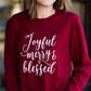 Woman standing out side of Inherit Clothing Company wearing a red and black, Joyful, Merry + Blessed Graphic Long Sleeve Tee.