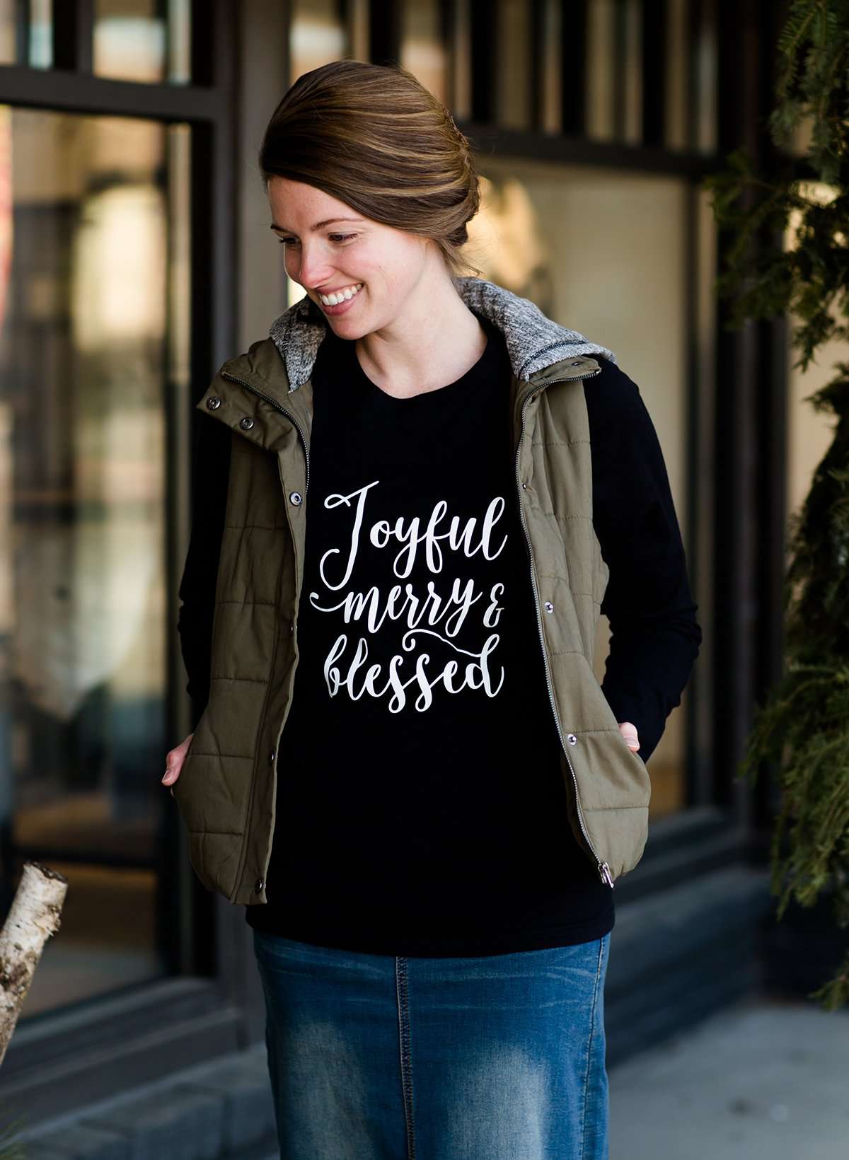 Woman standing out side of Inherit Clothing Company wearing a red and black, Joyful, Merry + Blessed Graphic Long Sleeve Tee.