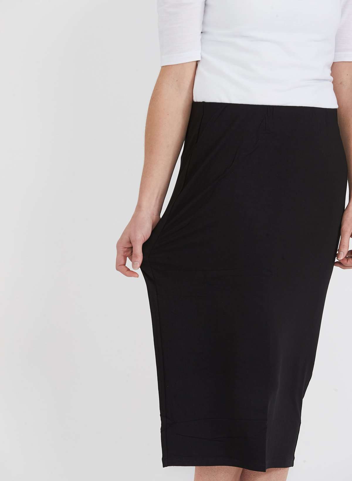 Woman wearing a straight style, ultra soft versatile black midi skirt.