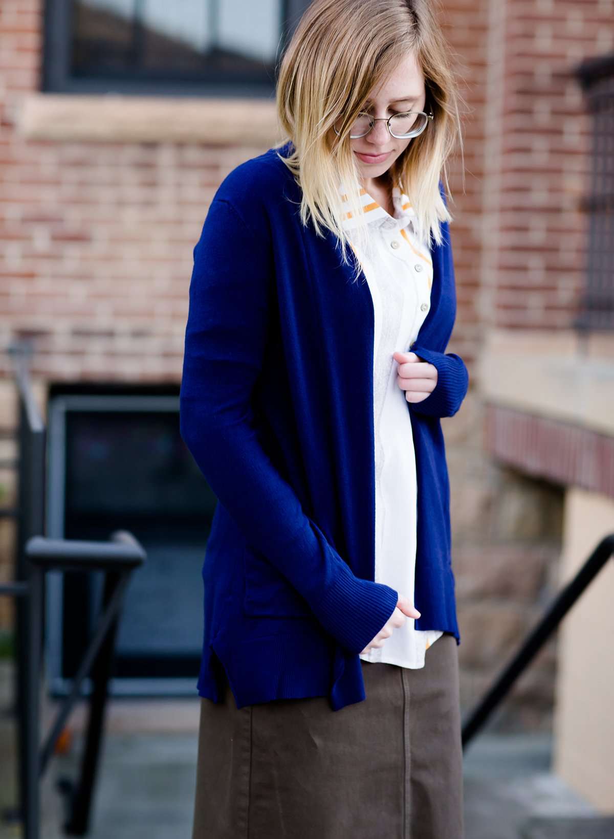 Young woman wearing a modest navy open front cardigan with front pockets and buttons over a mustard striped blouse