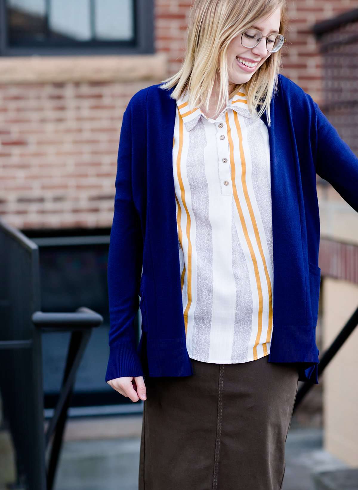 Young woman wearing a modest navy open front cardigan with front pockets and buttons over a mustard striped blouse