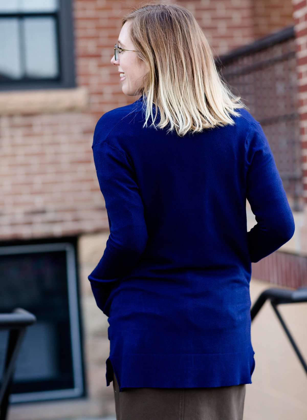 Young woman wearing a modest navy open front cardigan with front pockets and buttons over a mustard striped blouse