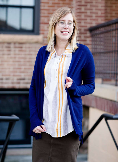 Young woman wearing a modest navy open front cardigan with front pockets and buttons over a mustard striped blouse