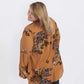 Plus size woman wearing a mustard floral lattice trim style tunic. This top is paired with a below the knee black skirt and leggings.