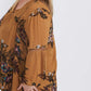 Plus size woman wearing a mustard floral lattice trim style tunic. This top is paired with a below the knee black skirt and leggings.