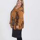 Plus size woman wearing a mustard floral lattice trim style tunic. This top is paired with a below the knee black skirt and leggings.