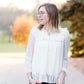 Young woman wearing a vintage inspired ruffle and layered cream colored blouse. This blouse features ruffles and ribbon details.