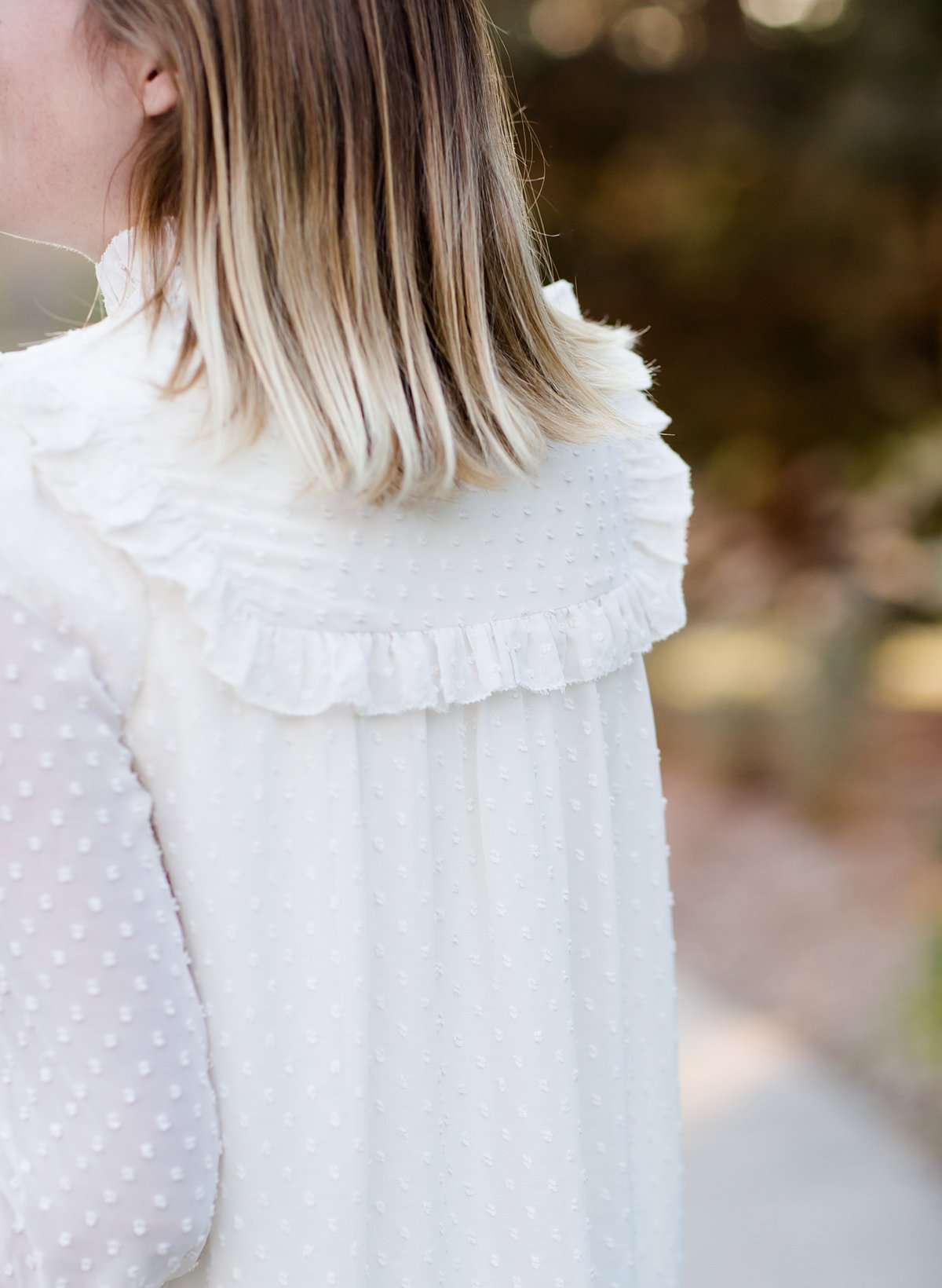 Young woman wearing a vintage inspired ruffle and layered cream colored blouse. This blouse features ruffles and ribbon details.