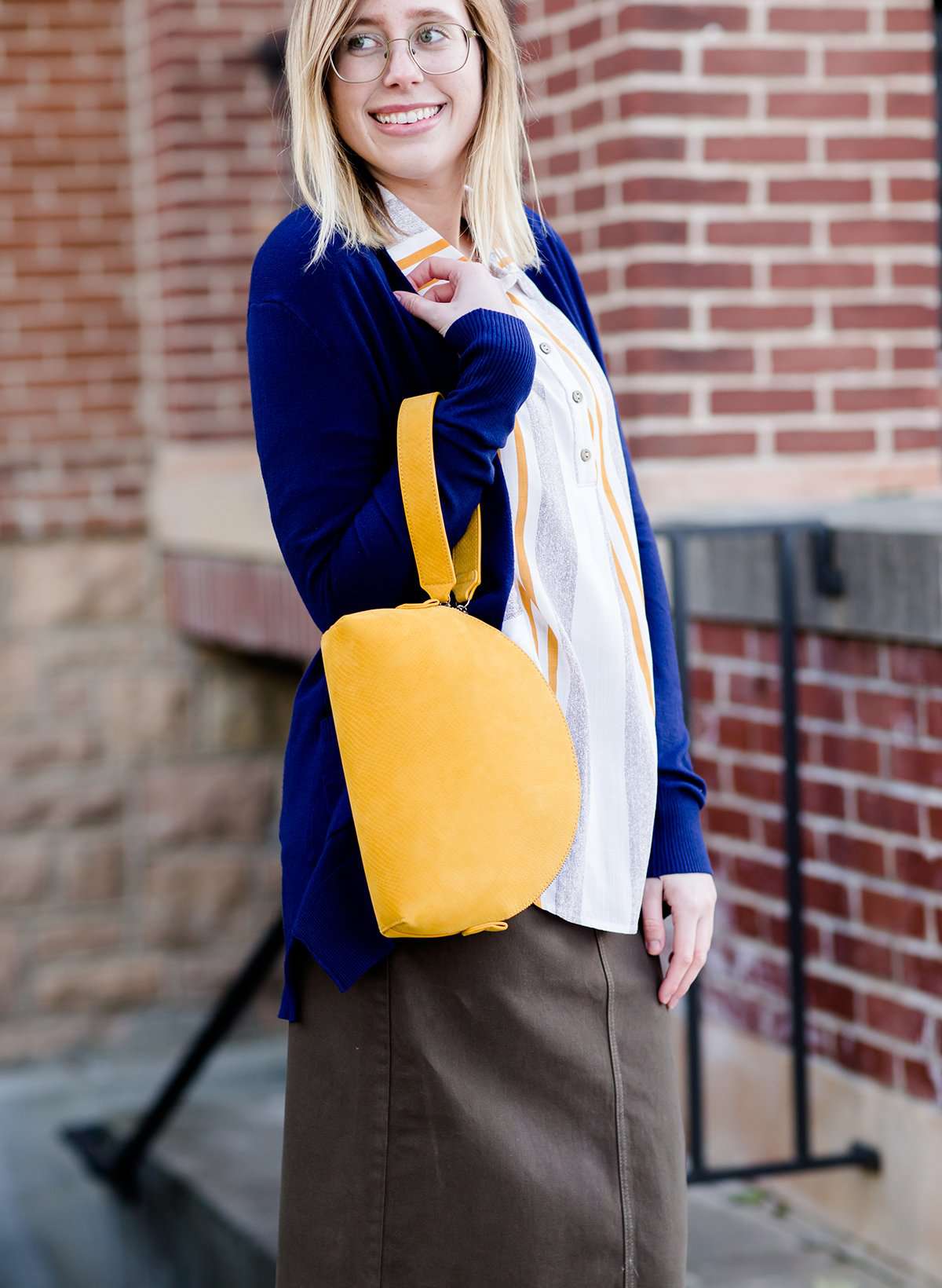 A faux leather crossbody bag. This bag has zippers and pockets along with a detachable strap. This is a mustard color with a slight snake print pattern.