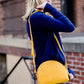 A faux leather crossbody bag. This bag has zippers and pockets along with a detachable strap. This is a mustard color with a slight snake print pattern.