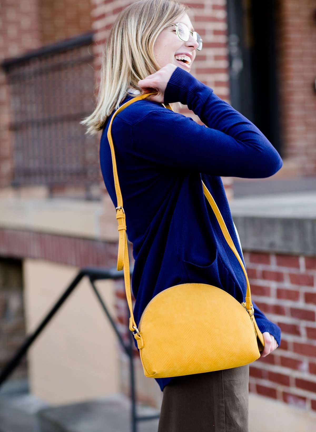 A faux leather crossbody bag. This bag has zippers and pockets along with a detachable strap. This is a mustard color with a slight snake print pattern.