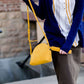 A faux leather crossbody bag. This bag has zippers and pockets along with a detachable strap. This is a mustard color with a slight snake print pattern.