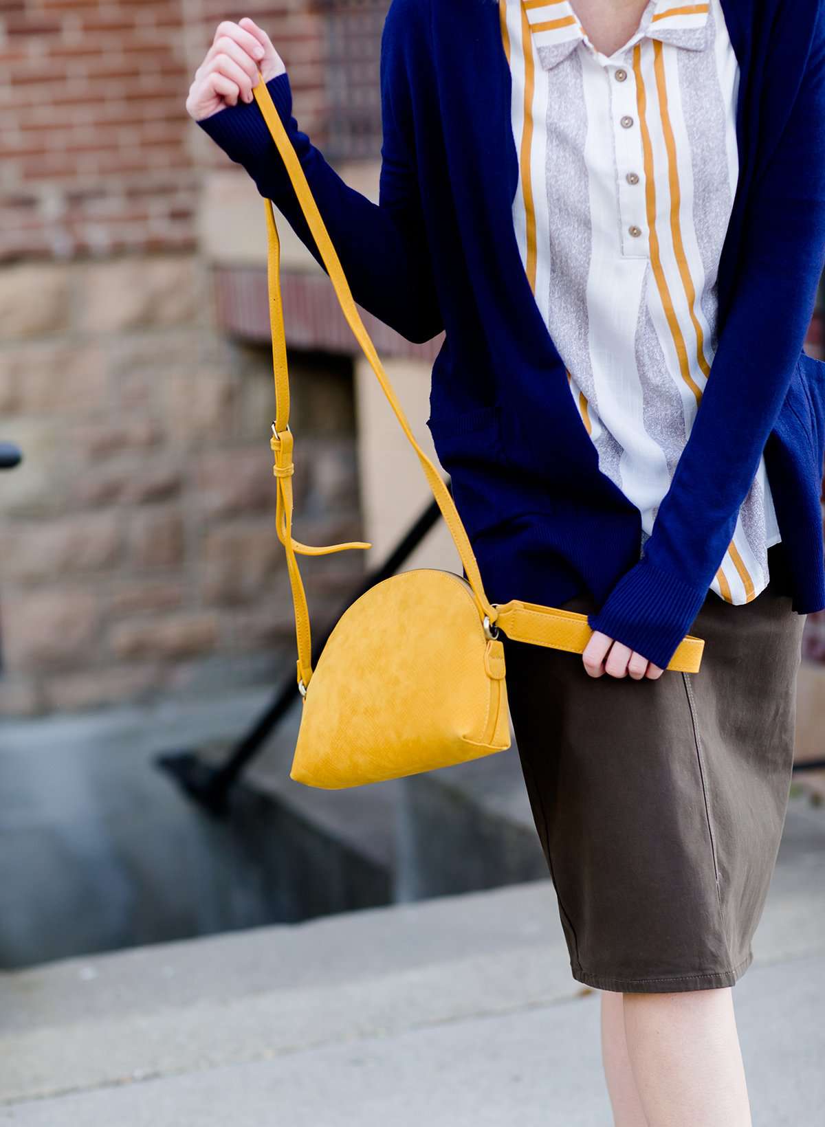 A faux leather crossbody bag. This bag has zippers and pockets along with a detachable strap. This is a mustard color with a slight snake print pattern.