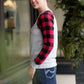 Model woman wearing a grey long sleeve tee with buffalo plaid sleeves and the script font that reads Merry Christmas. 