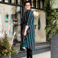 Modest woman wearing a green and black striped midi dress with a self tie bow. She is wearing black leggings and black booties as well. She is at Inherit Clothing Company.
