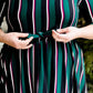 Modest woman wearing a green and black striped midi dress with a self tie bow. She is wearing black leggings and black booties as well. She is at Inherit Clothing Company.
