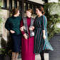 Modest woman wearing a green and black striped midi dress with a self tie bow. She is wearing black leggings and black booties as well. She is at Inherit Clothing Company.