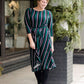 Modest woman wearing a green and black striped midi dress with a self tie bow. She is wearing black leggings and black booties as well. She is at Inherit Clothing Company.