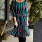 Modest woman wearing a green and black striped midi dress with a self tie bow. She is wearing black leggings and black booties as well. She is at Inherit Clothing Company.